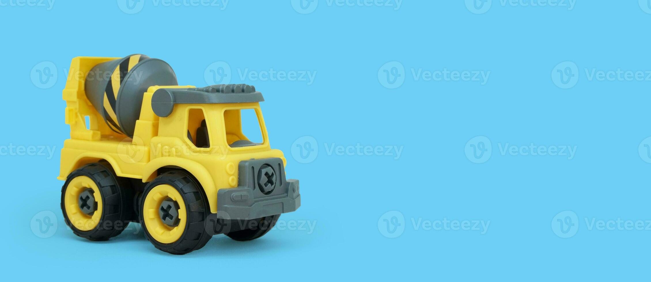 Yellow plastic concrete mixer truck toy isolated on blue background with copy space for banner of toy store. photo