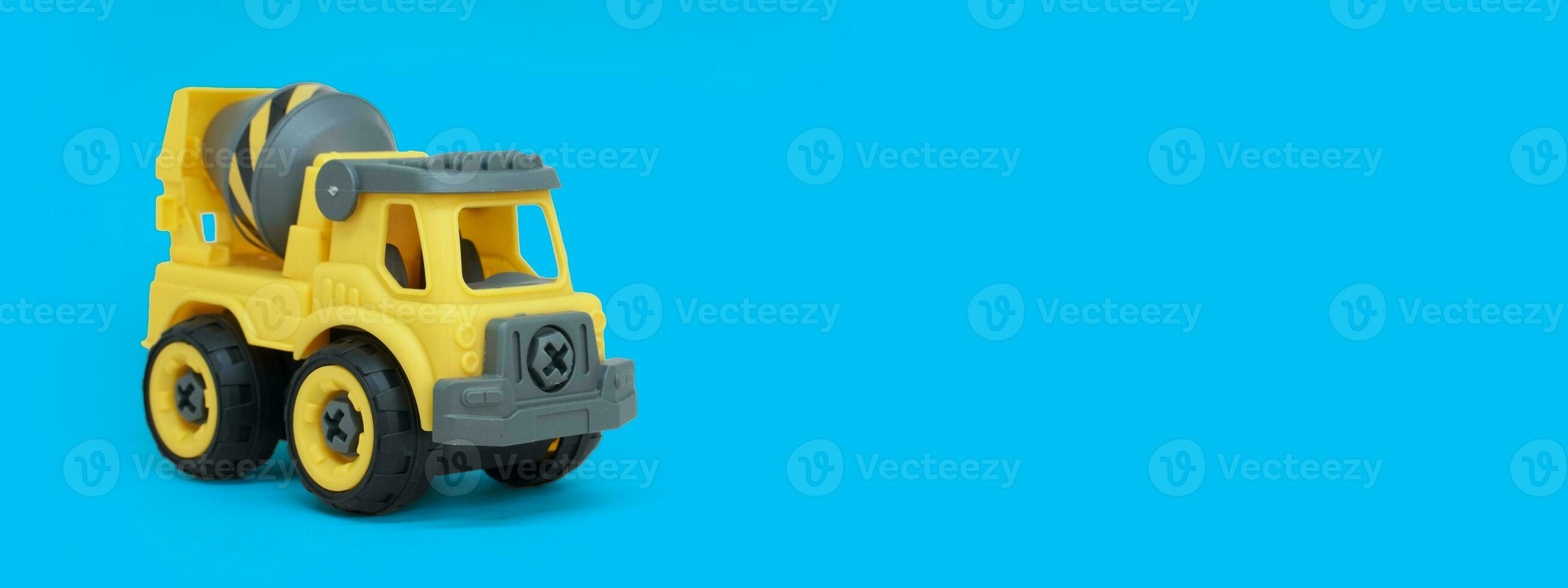 Yellow plastic concrete mixer truck toy isolated on blue background. construction vechicle truck. a copy space for banner of toy store. photo