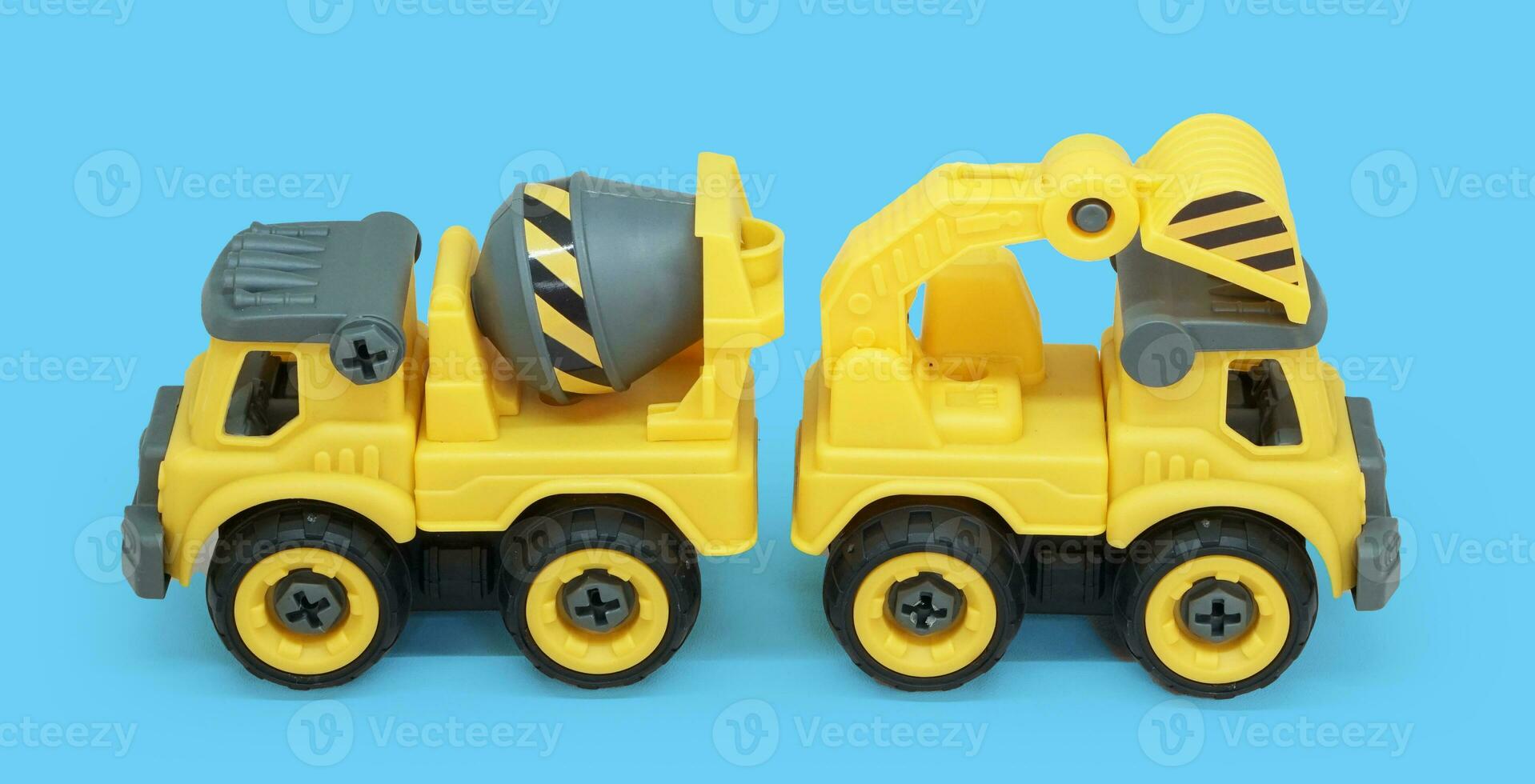 side view yellow plastic toy of concrete mixer and ecavator truck isolated on blue background. heavy construction vehicle. photo