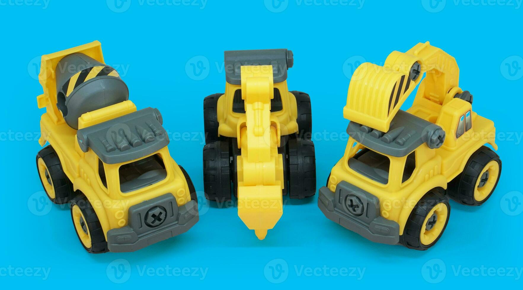 yellow plastic toy of concrete mixer, tractor drill and excavator truck line up isolated on blue background. heavy construction vehicle. photo