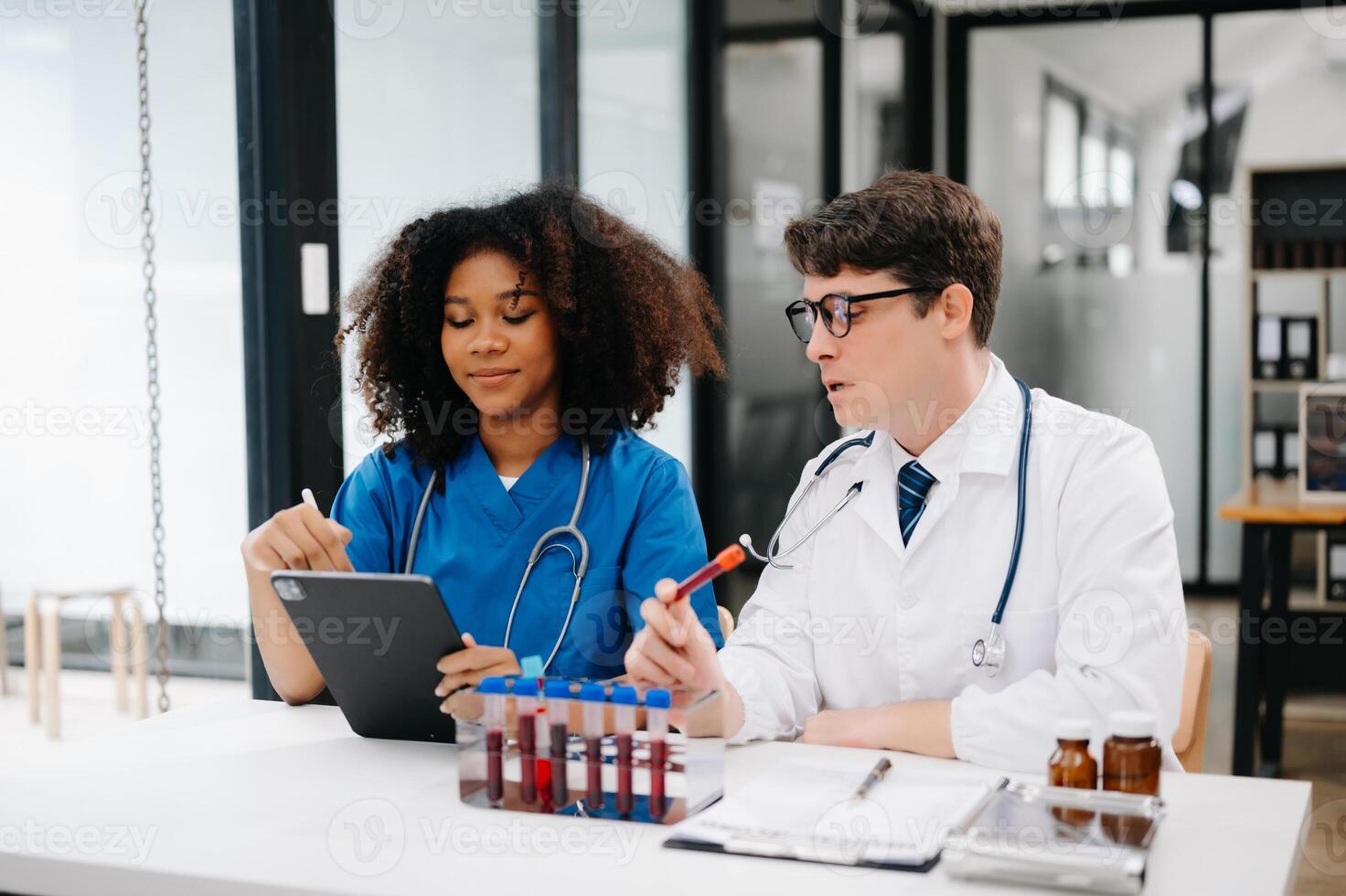 Doctor Talks With Professional Head Nurse or Surgeon, They Use Digital tablet Computer. Diverse Team of Health Care Specialists Discussing Test Result on desk in hospital photo