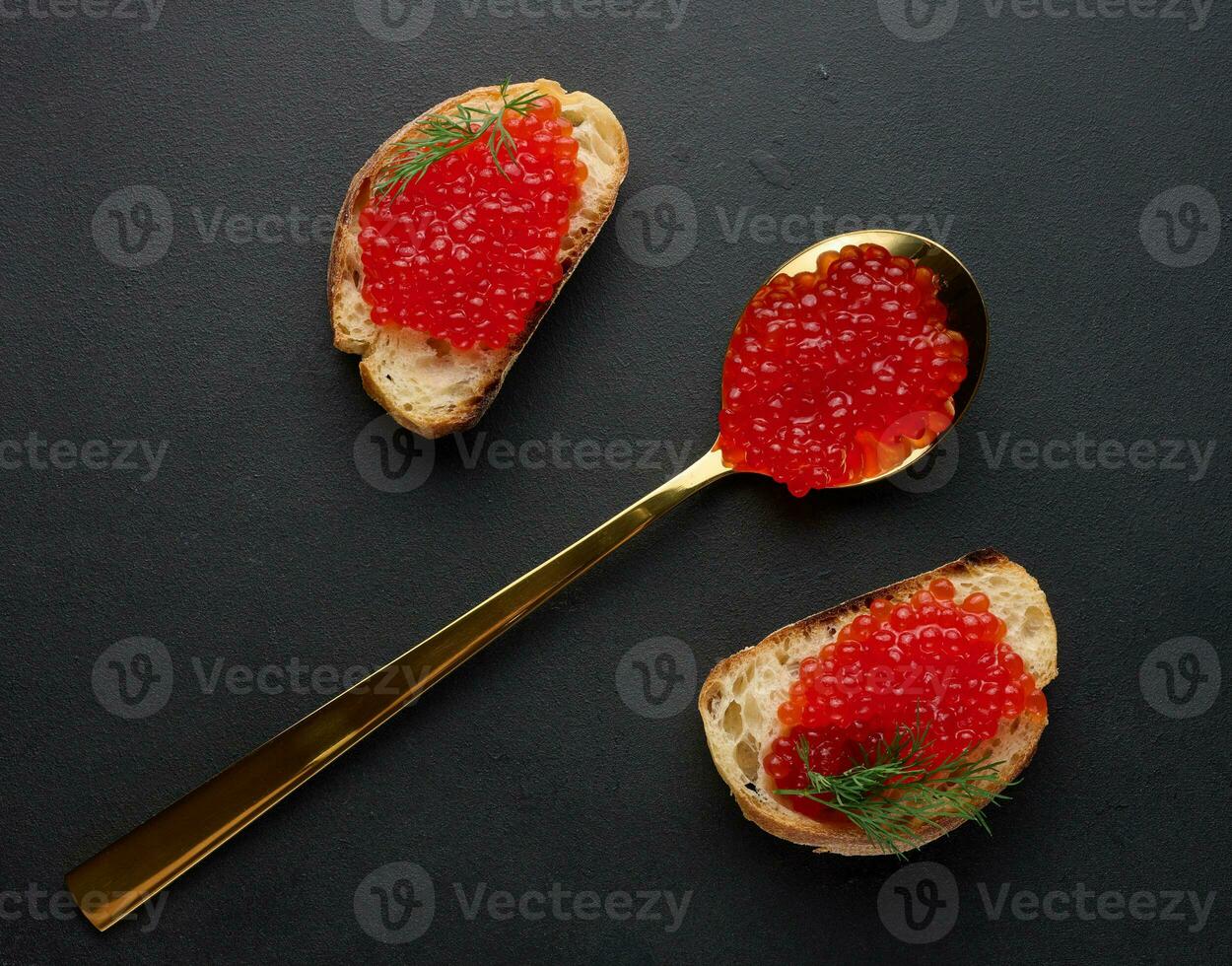 rojo caviar en rebanadas de blanco trigo un pan en un negro mesa, concepto de lujo y gastrónomo cocina foto