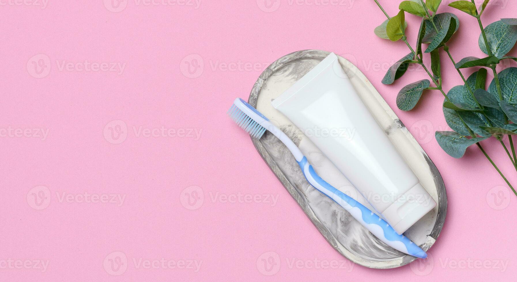 White plastic toothpaste tube and toothbrush on a pink background. Copy space photo