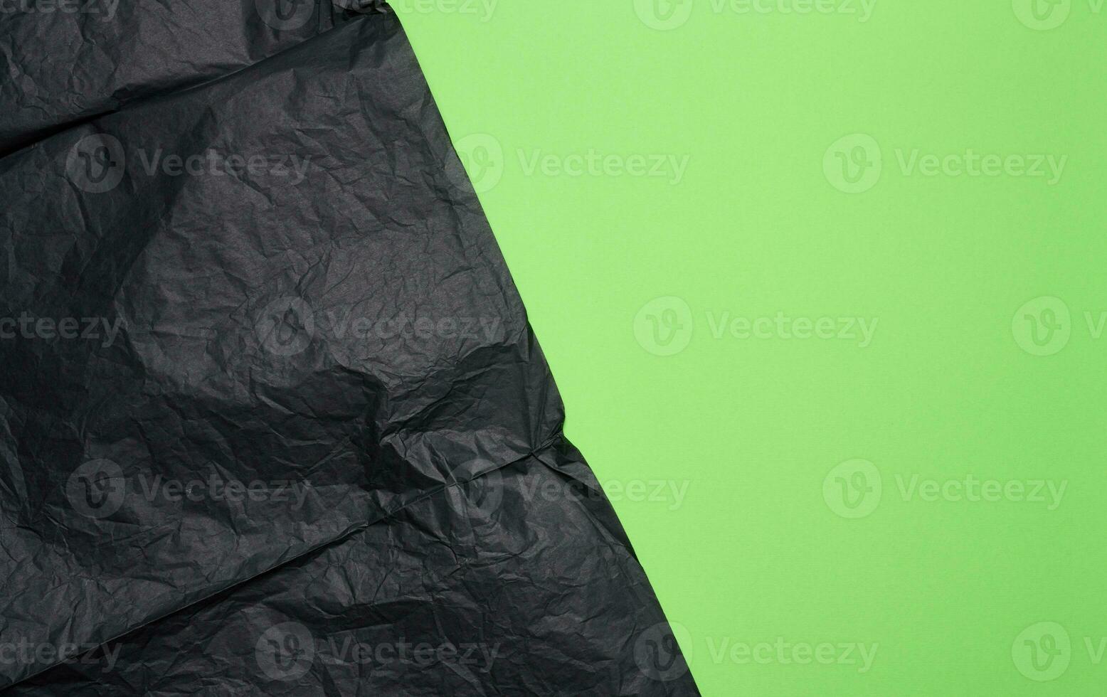 Crumpled sheet of black parchment paper, green background photo