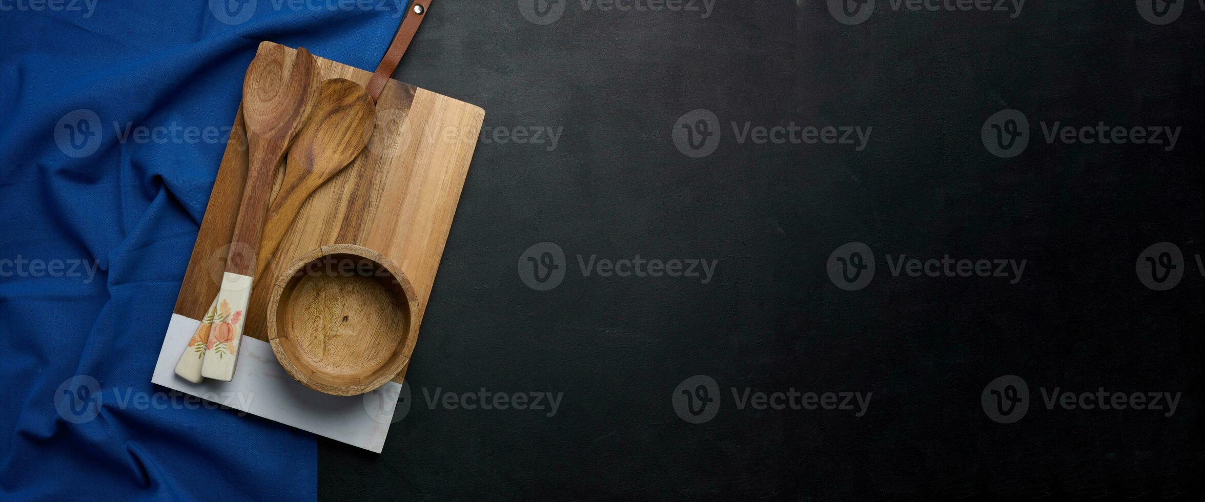Empty rectangular wooden kitchen cutting board, empty bowl and wooden spoons on black table top view photo
