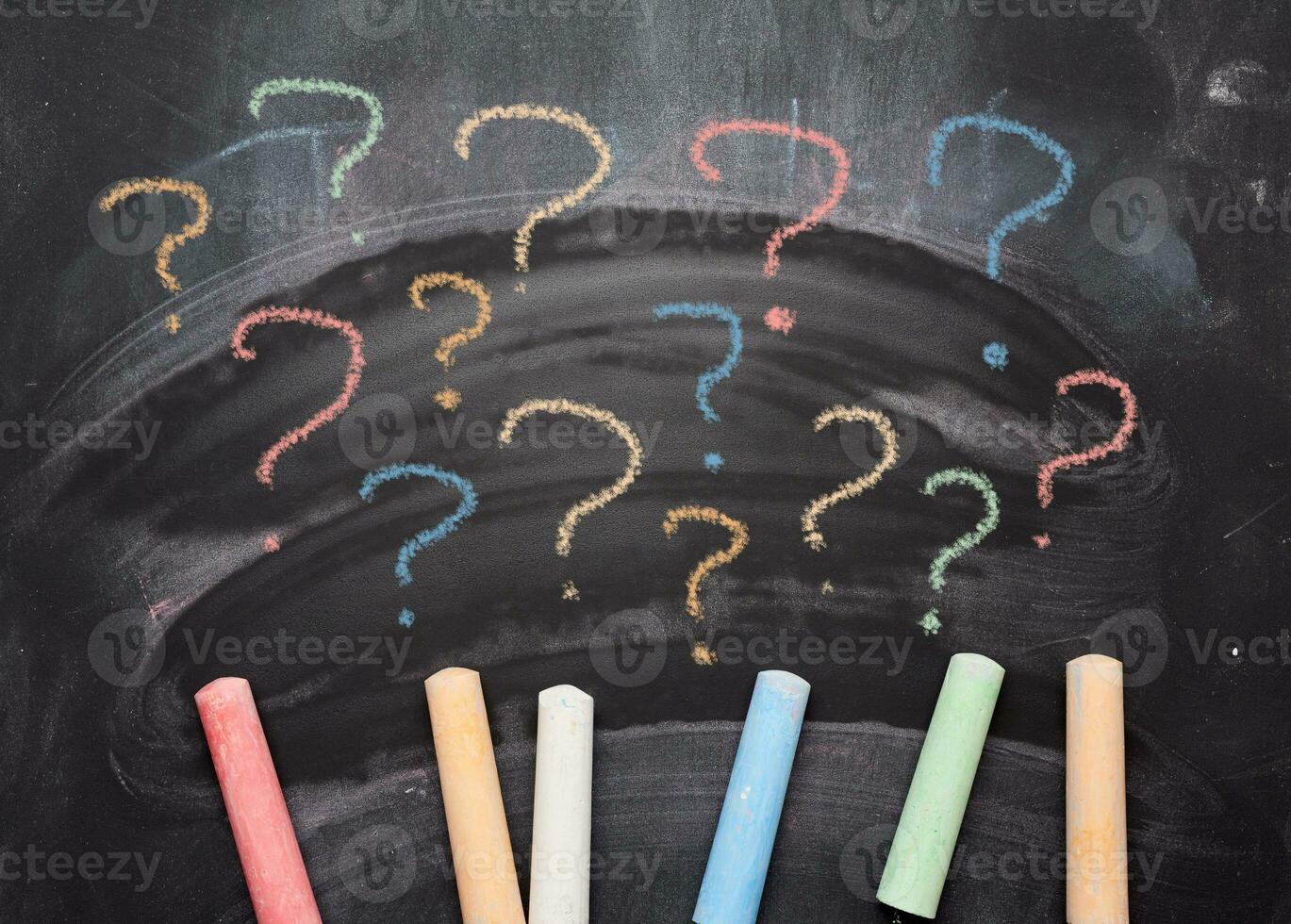 Multicolored crayons on a black chalk board and drawn question marks. Searching of decisions photo