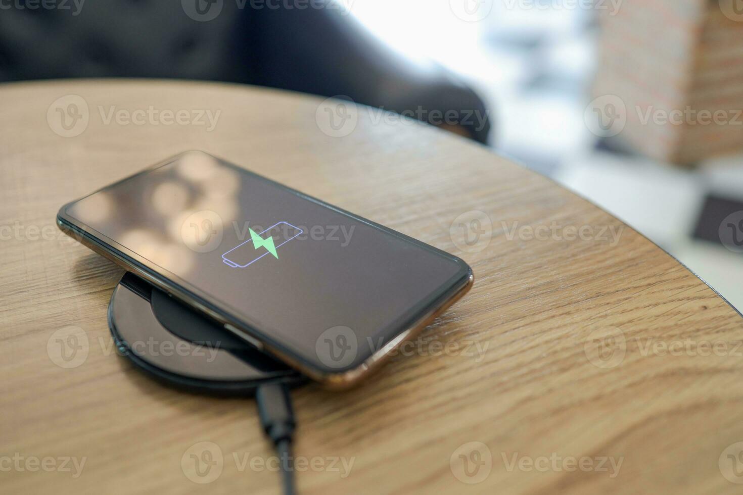 Charging mobile phone battery with wireless charging device in the table. Smartphone charging on a charging pad. Mobile phone near wireless charger Modern lifestyle concept. photo