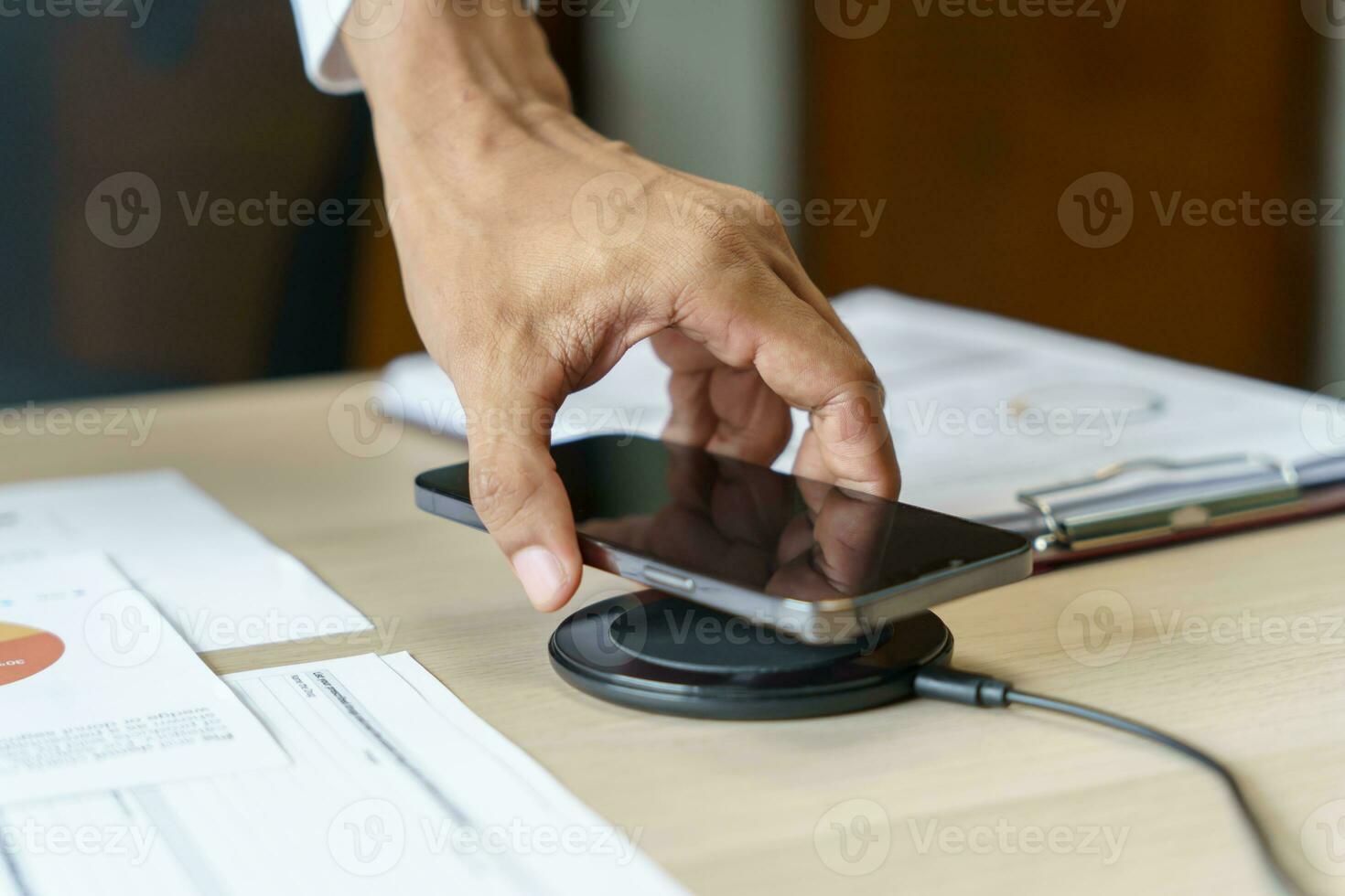 Charging mobile phone battery with wireless charging device in the table. Smartphone charging on a charging pad. Mobile phone near wireless charger Modern lifestyle technology concept photo