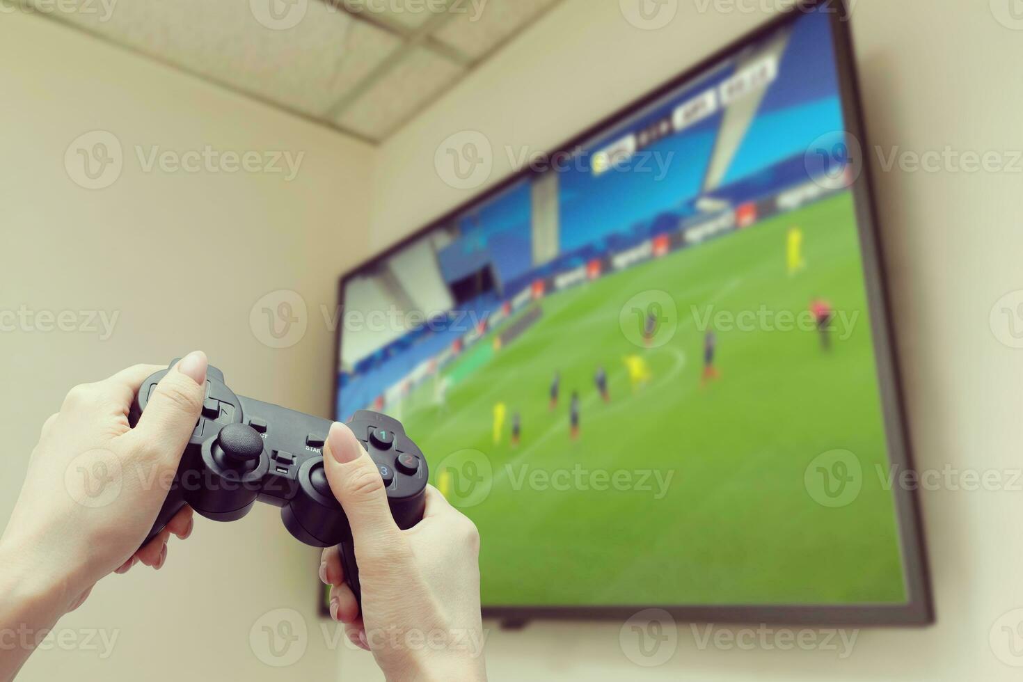 woman playing video game. Hands holding console controller. Football or soccer game on the television. Widescreen tv stands on commode. photo