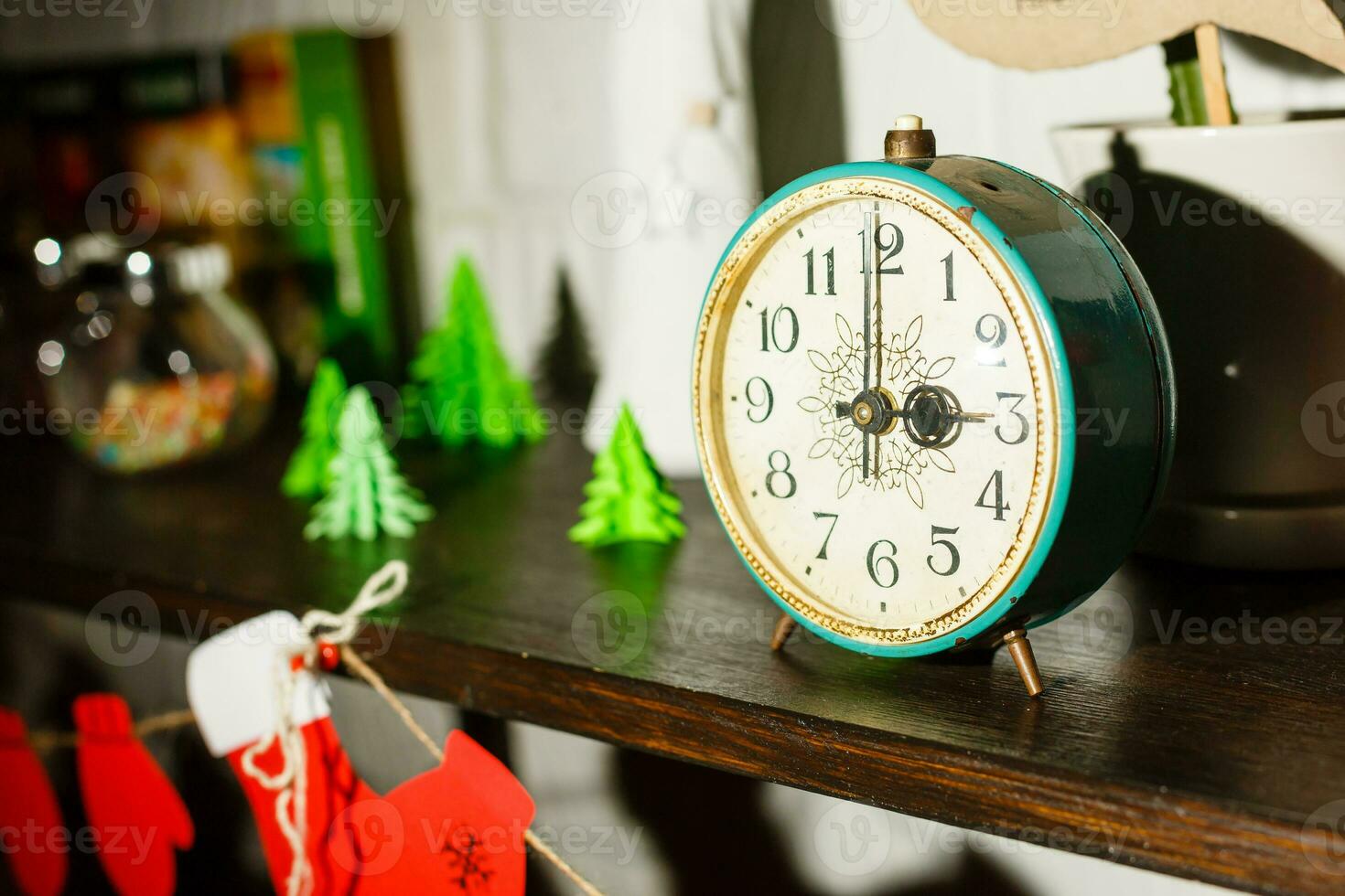 New Year and Christmas theme. Vintage alarm clock on a shelf with Santa red sock and miniature Christmas trees photo