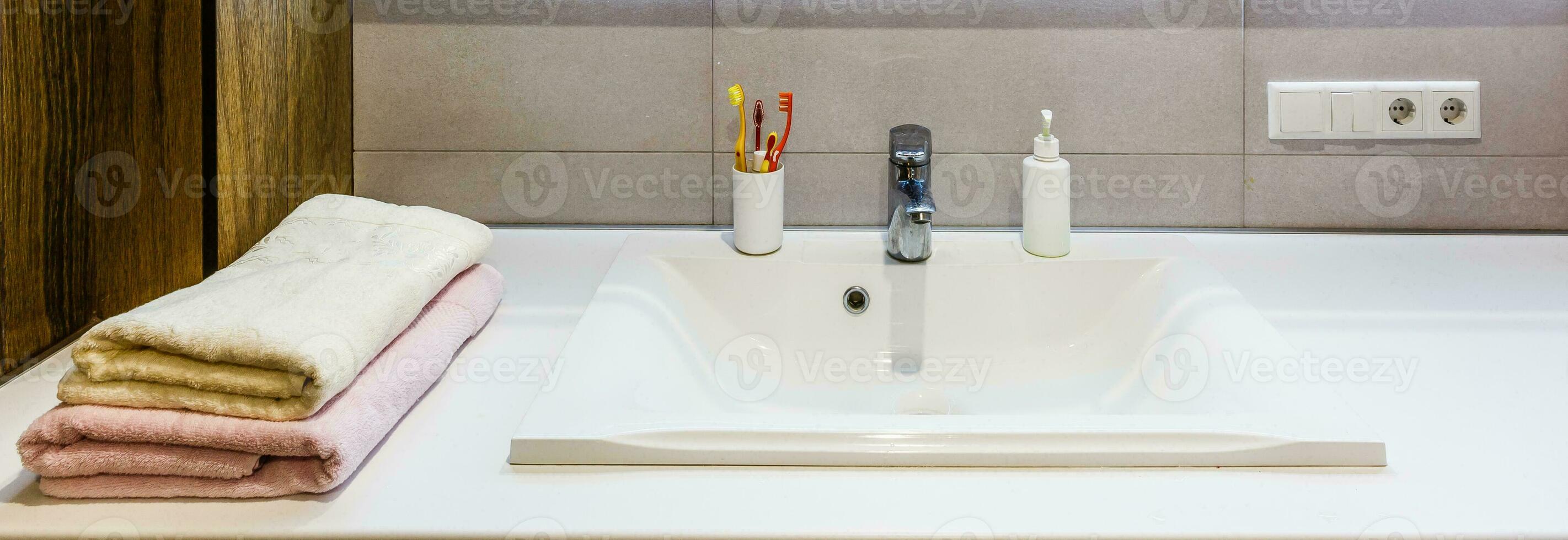 White and brown bathroom boasts a nook filled with double vanity cabinet topped with white and grey counter paired with tile backsplash under framed mirror photo