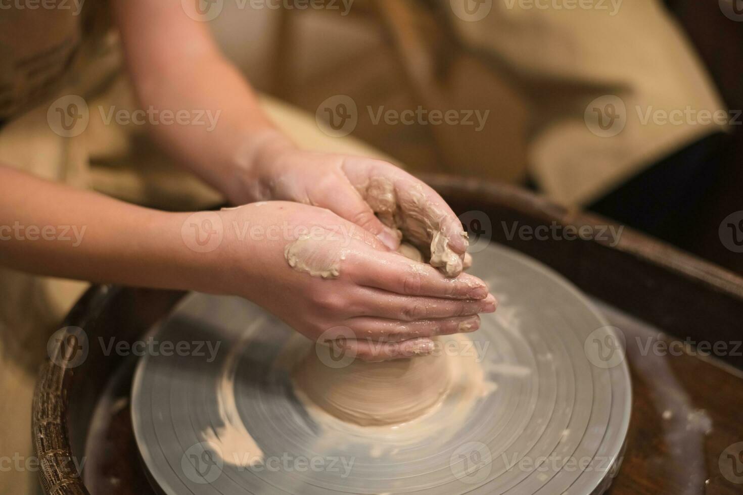 Potter girl works on potter's wheel, making ceramic pot out of clay in pottery workshop photo