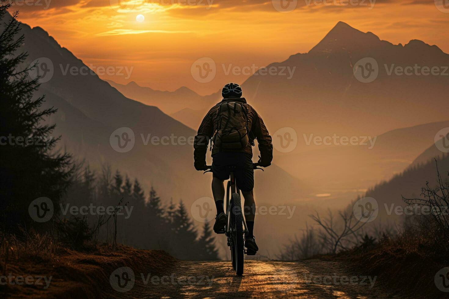 Back view silhouette of a traveler on a mountain bike in the orange lights of the sunrise going down a foggy mountain valley photo