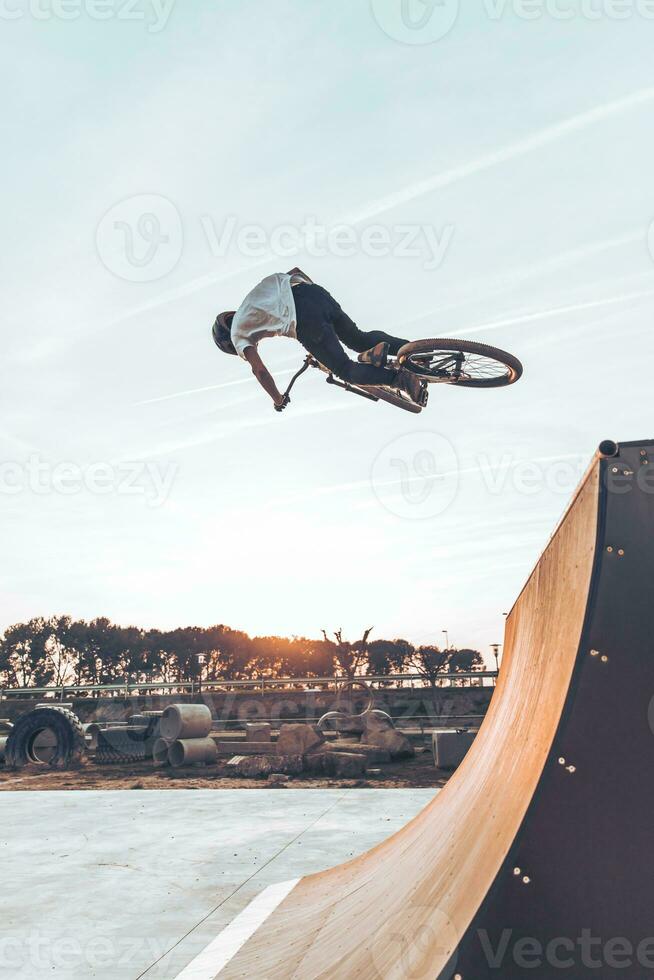 Carefree man performing stunt with bicycle on ramp against sky in park at sunset photo