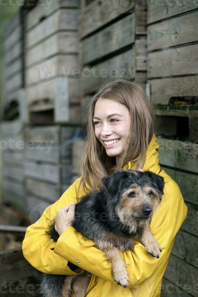 Smiling woman on a farm standing at wooden boxes holding dog photo