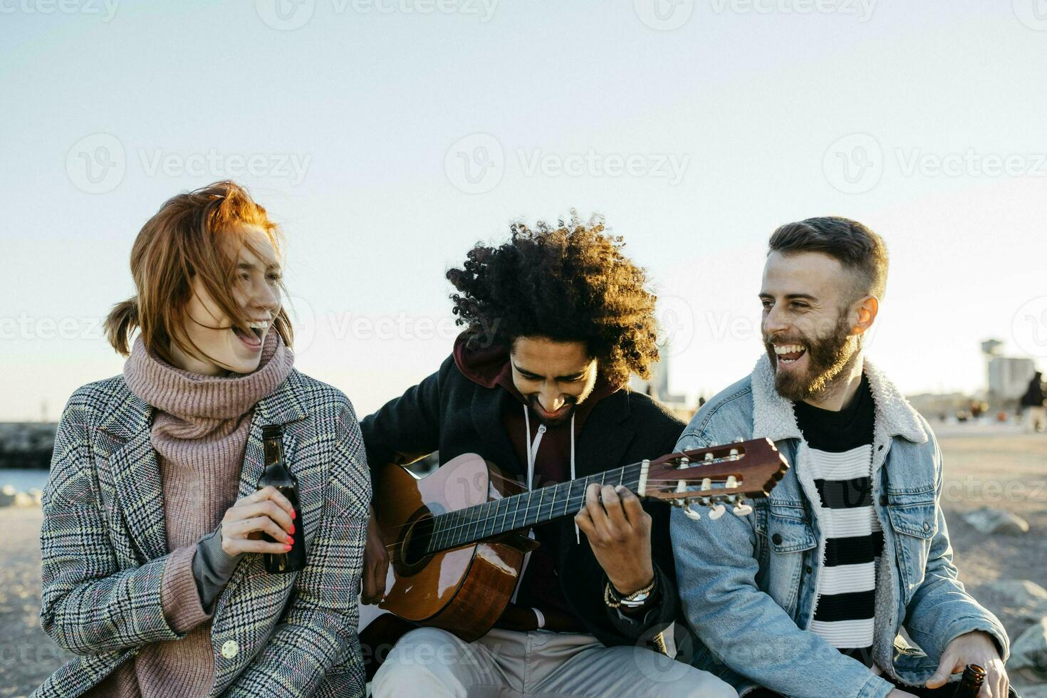 Three happy friends with guitar sitting outdoors at sunset photo