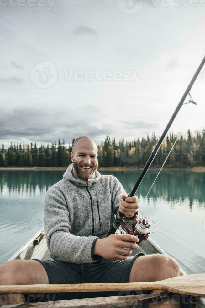 Canada, British Columbia, portrait of happy man fishing in canoe on Boya Lake photo