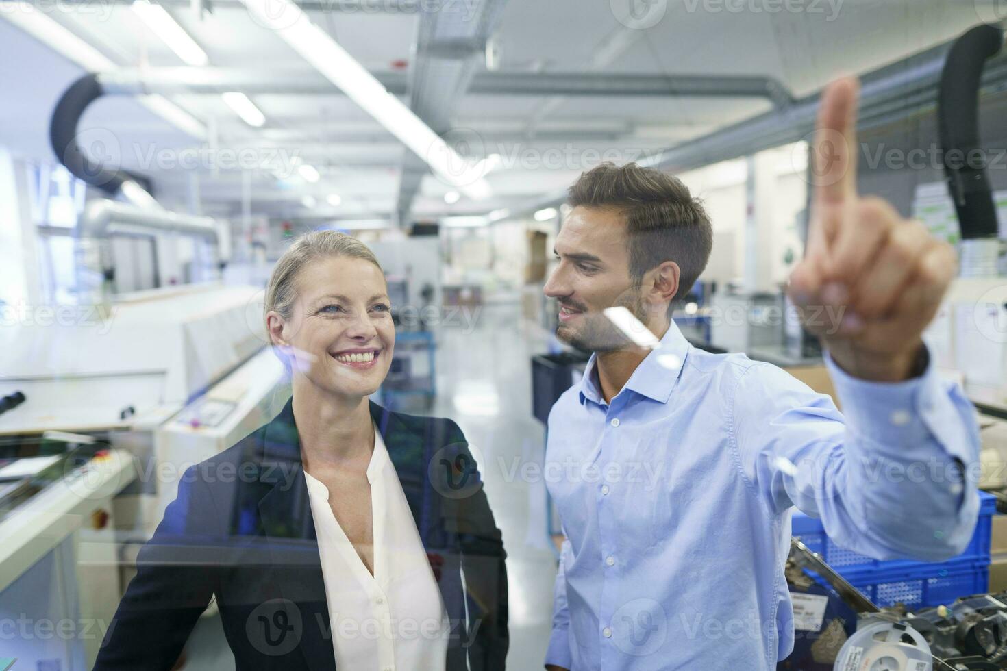 Young male technician pointing at graphical interface on glass in factory photo