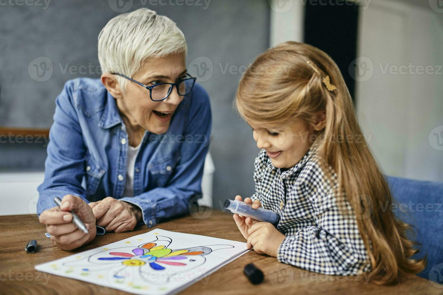 Grandmother and granddaughter sitting at table, painting colouring book photo