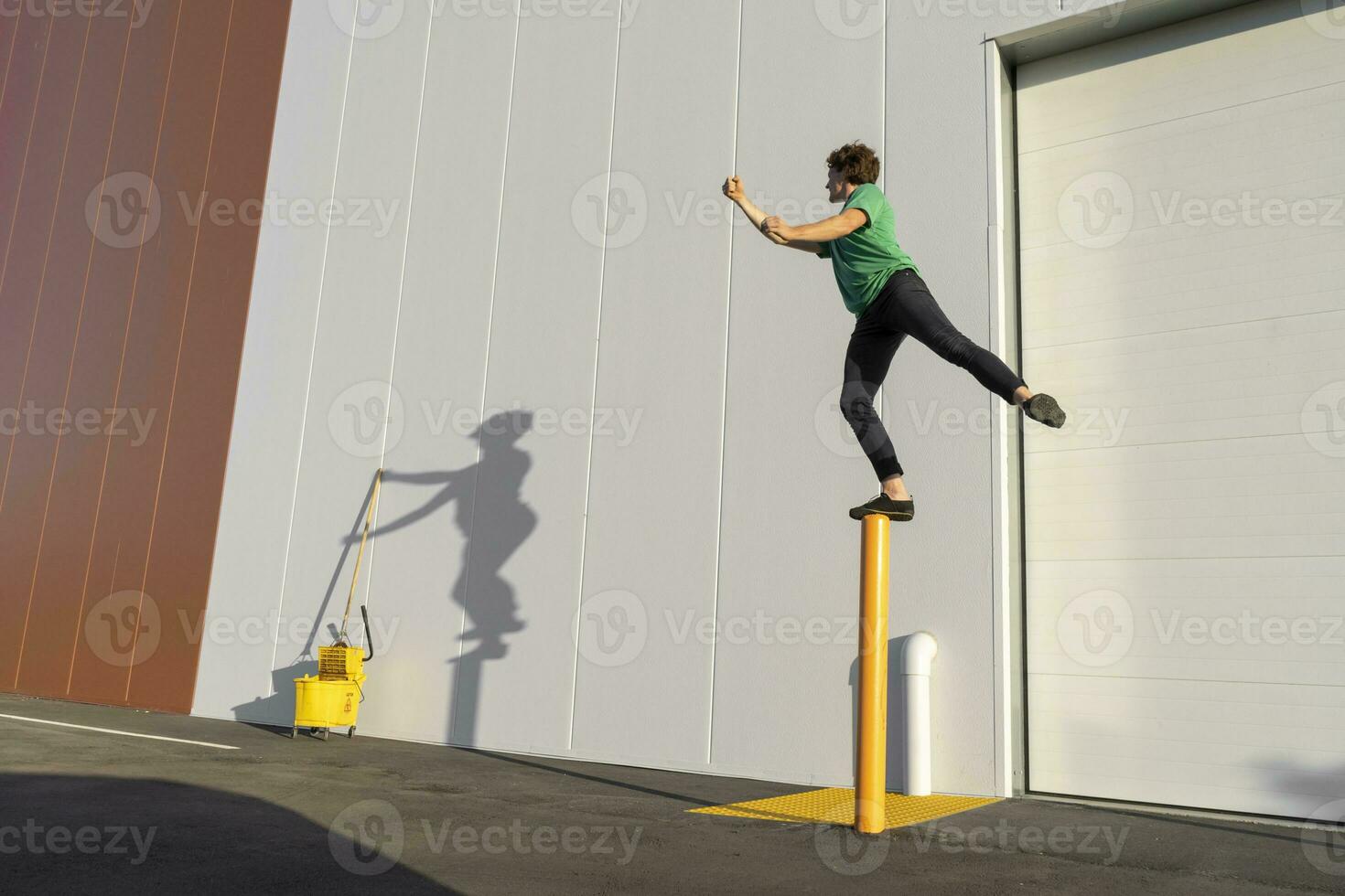 Acrobat standing on pole, casting shadow at cleaning bucket photo