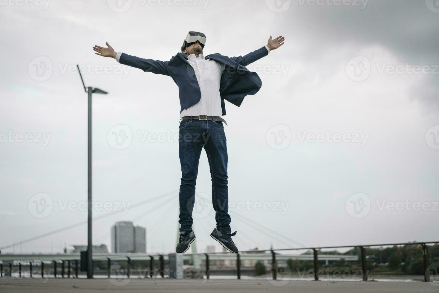 Businessman wearing VR glasses jumping in the city photo