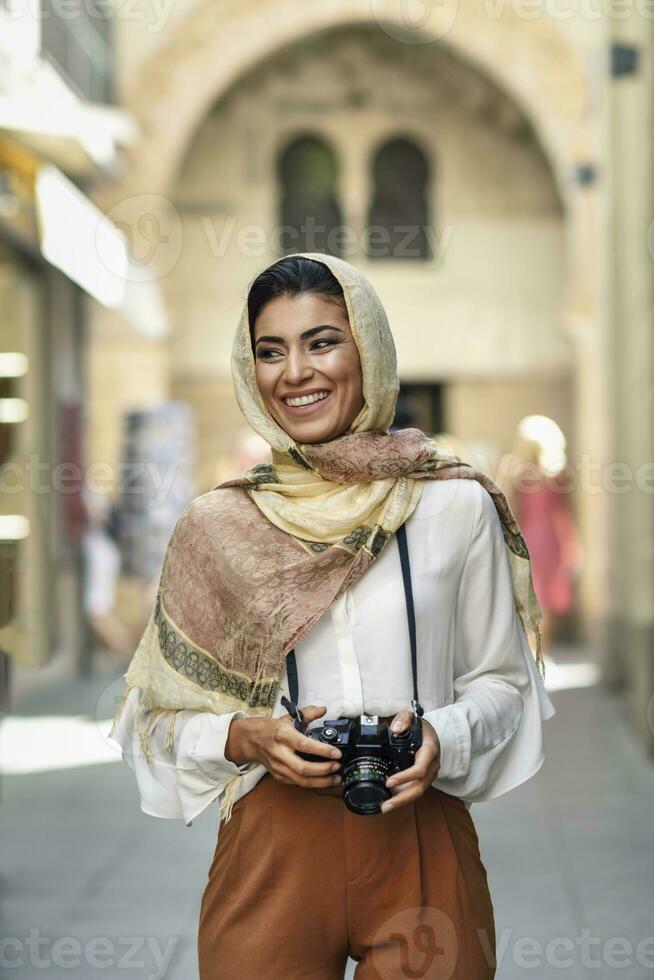 Spain, Granada, young Arab tourist woman wearing hijab, using camera during sightseeing in the city photo