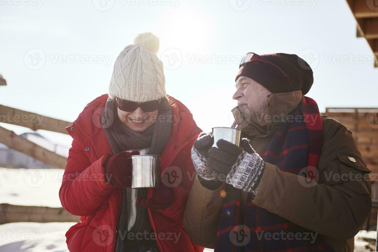 Happy mature couple with hot drinks outdoors at mountain hut in winter photo