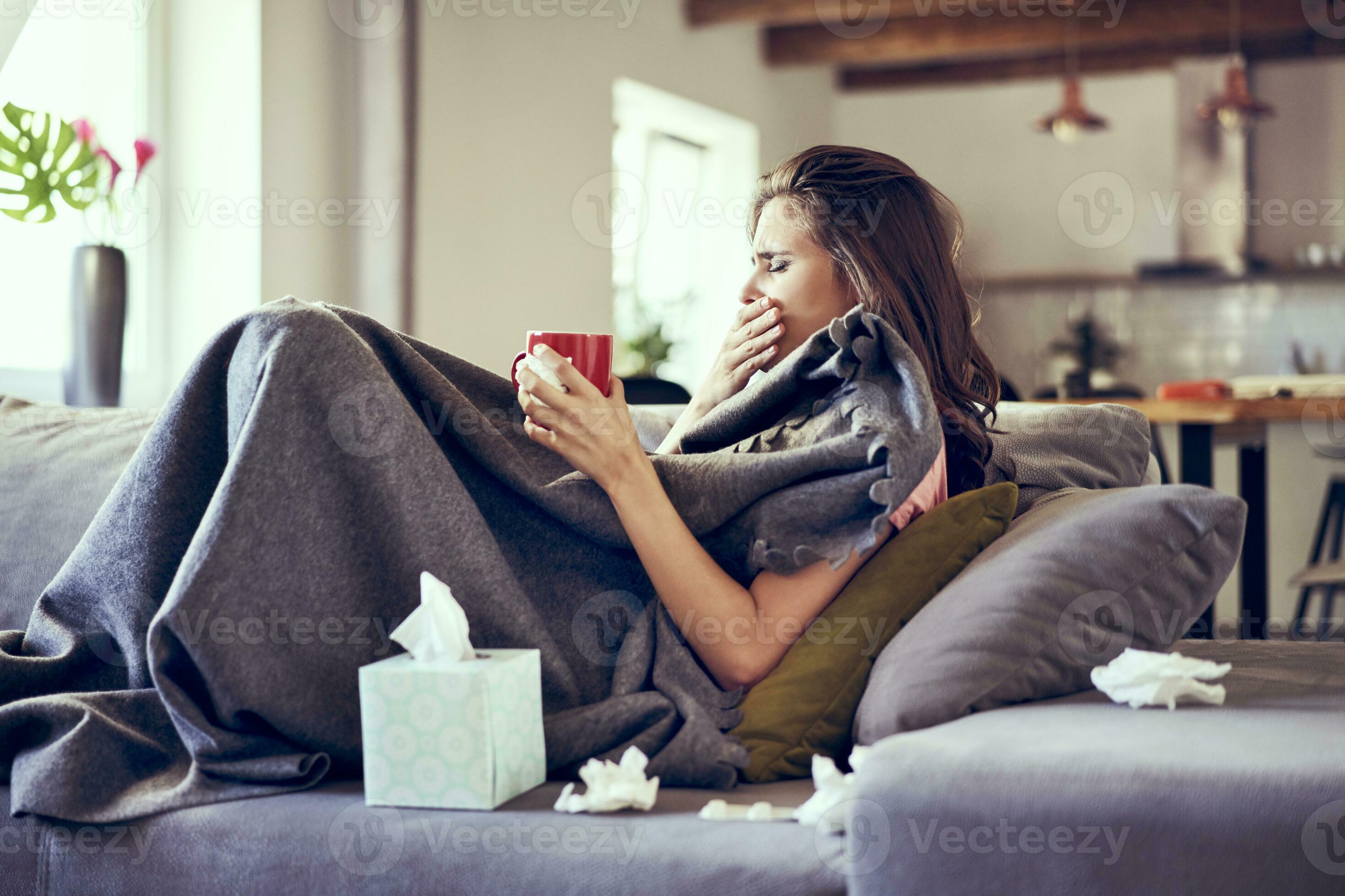 Portrait of woman lying sick on sofa coughing and trying to drink hot