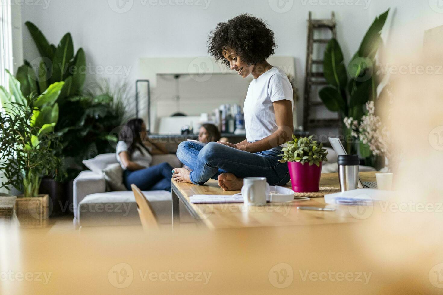 Smiling woman using tablet on table at home with friends in background photo