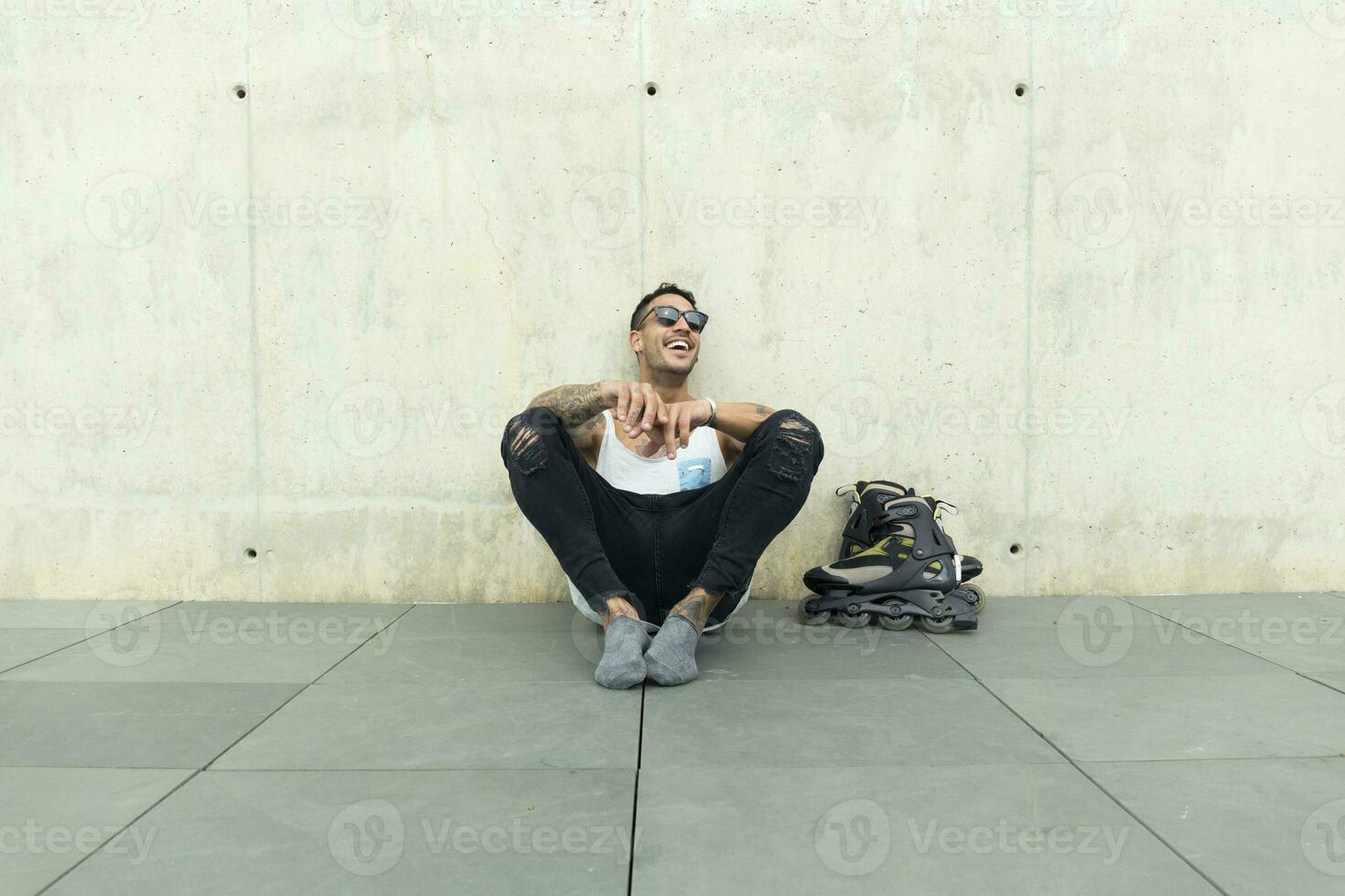 Tattooed young man with roller skates sitting on ground having fun photo