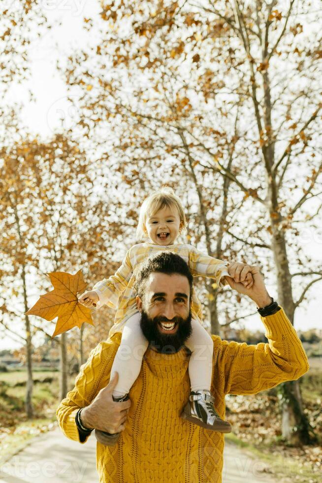 padre que lleva su pequeño hija en espalda en el Mañana en un parque en otoño foto