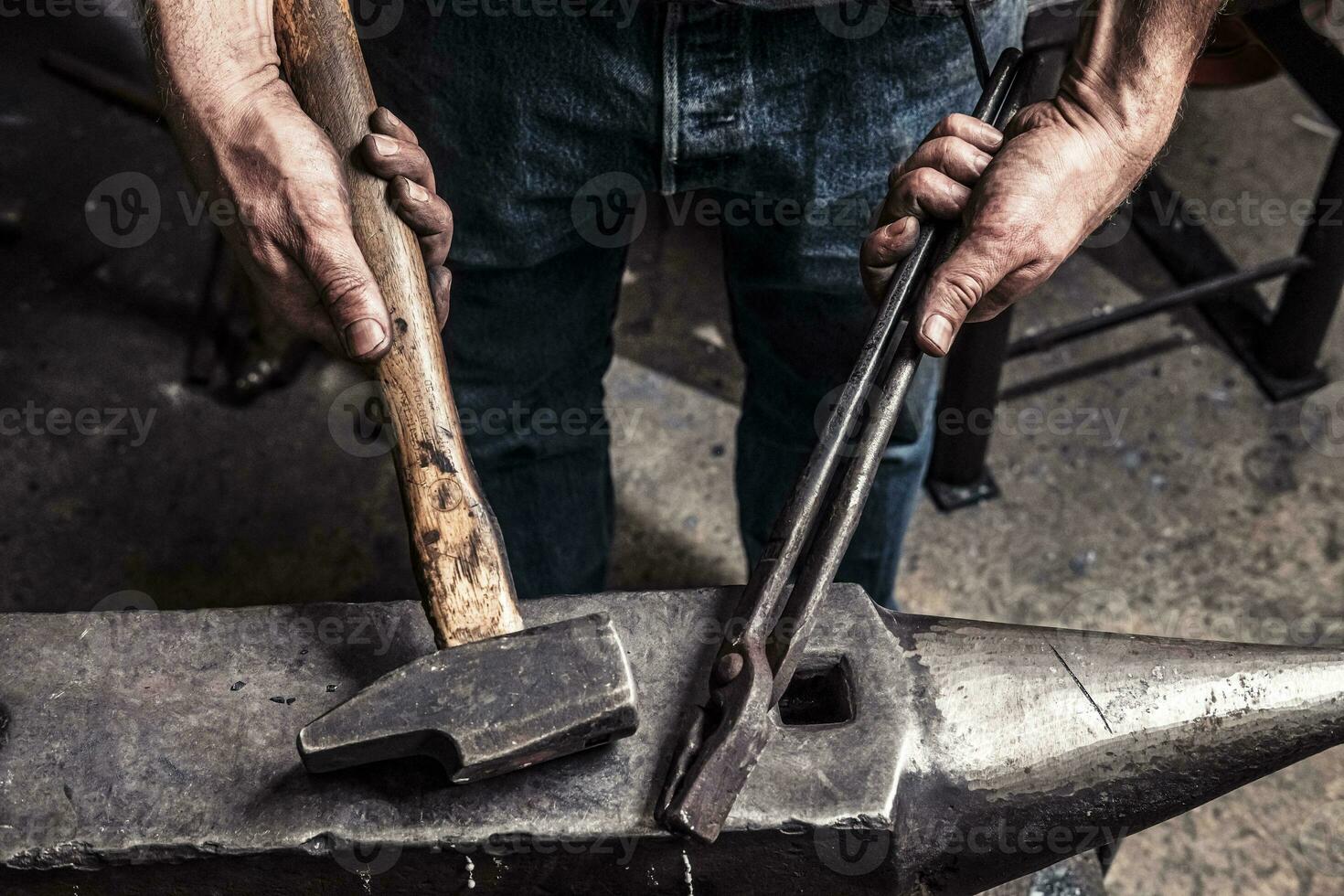 Knife maker holding pliers and hammer on anvil photo