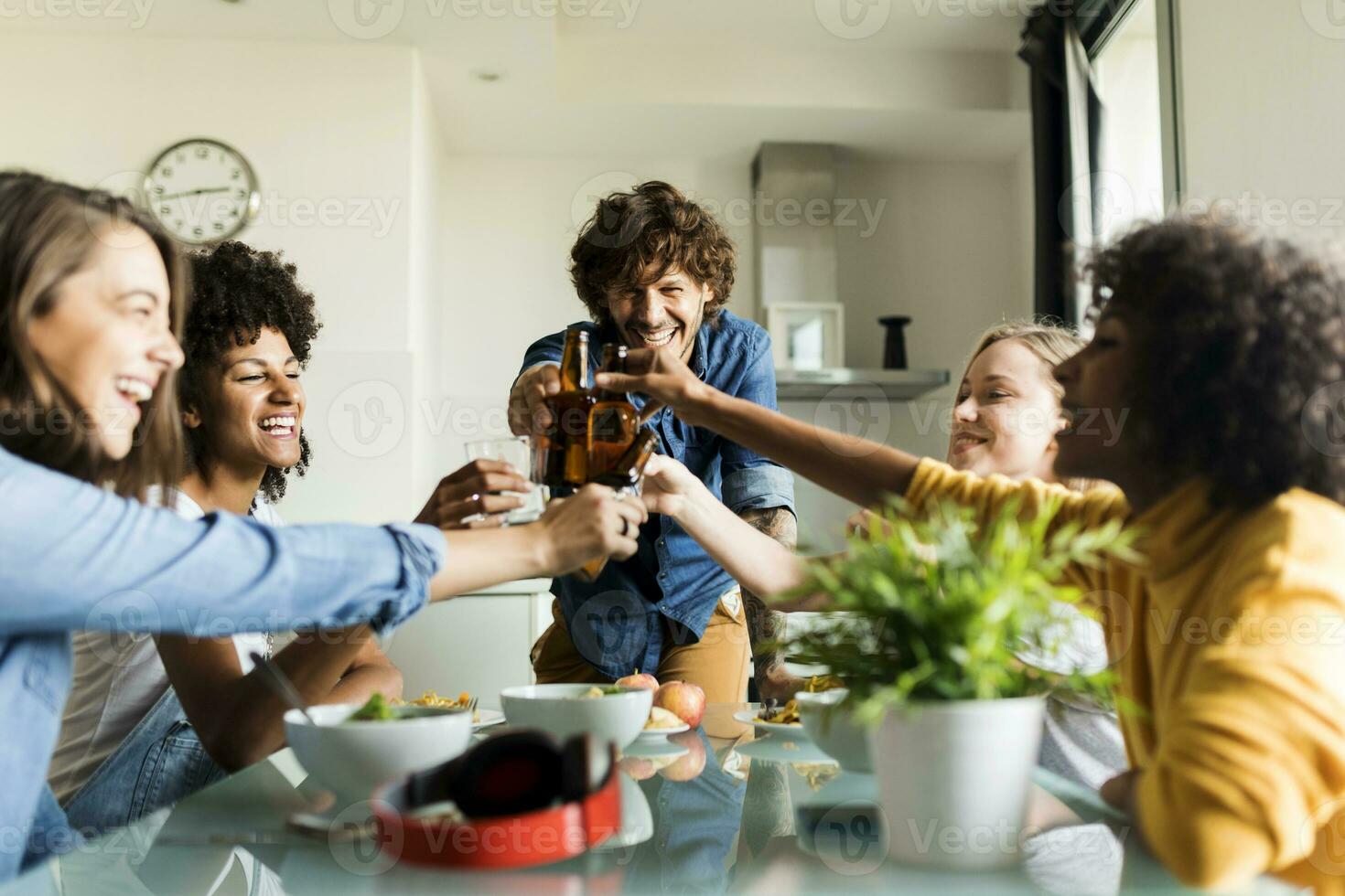 Cheerful friends clinking beer bottles at dining table photo