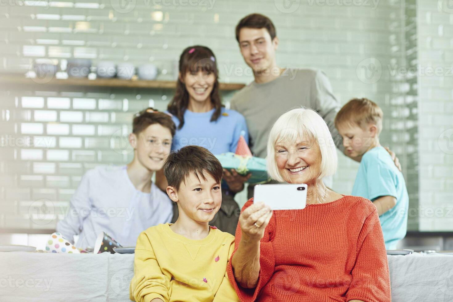 Mother and sons celebrating grandmother's bithday in their kitchen, boy taking selfies photo