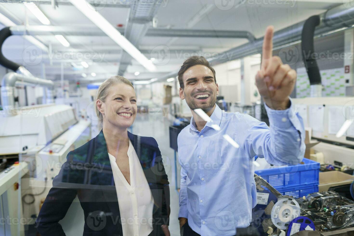 Happy young male technician pointing at graphical interface on glass in factory photo