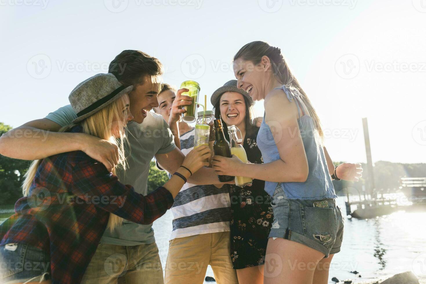 Group of happy friends standing at the riverside toasting with drinks photo