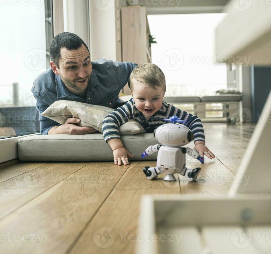 Excited father and son lying on a mattress at home watching a toy robot photo
