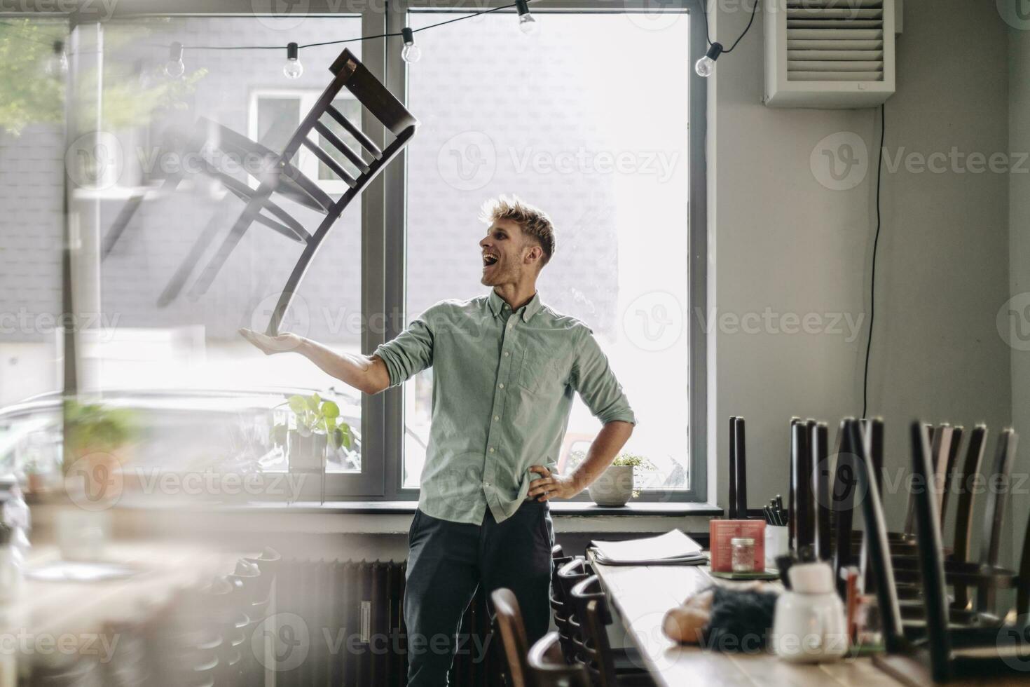 Man balancing chair on his hand, closing his coffee shop photo