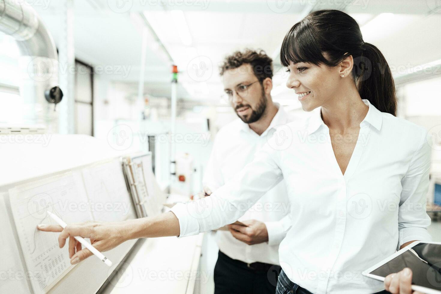 Smiling female technician pointing at graph while discussing with male colleague at laboratory photo