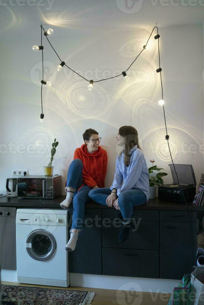 Two girlfriends at home sitting in kitche, talking and drinking tea photo