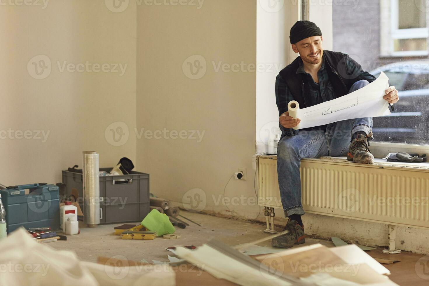 Man refurbishing shop location, sitting on windowsill, studying blueprint photo