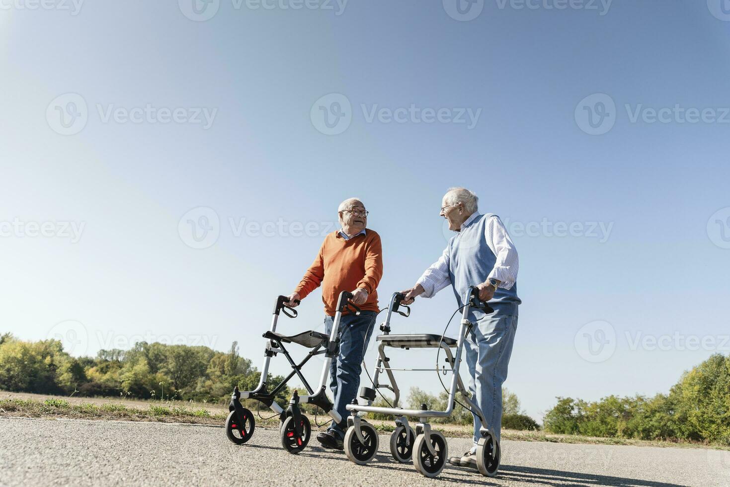 Two old friends walking on a country road, using wheeled walkers photo