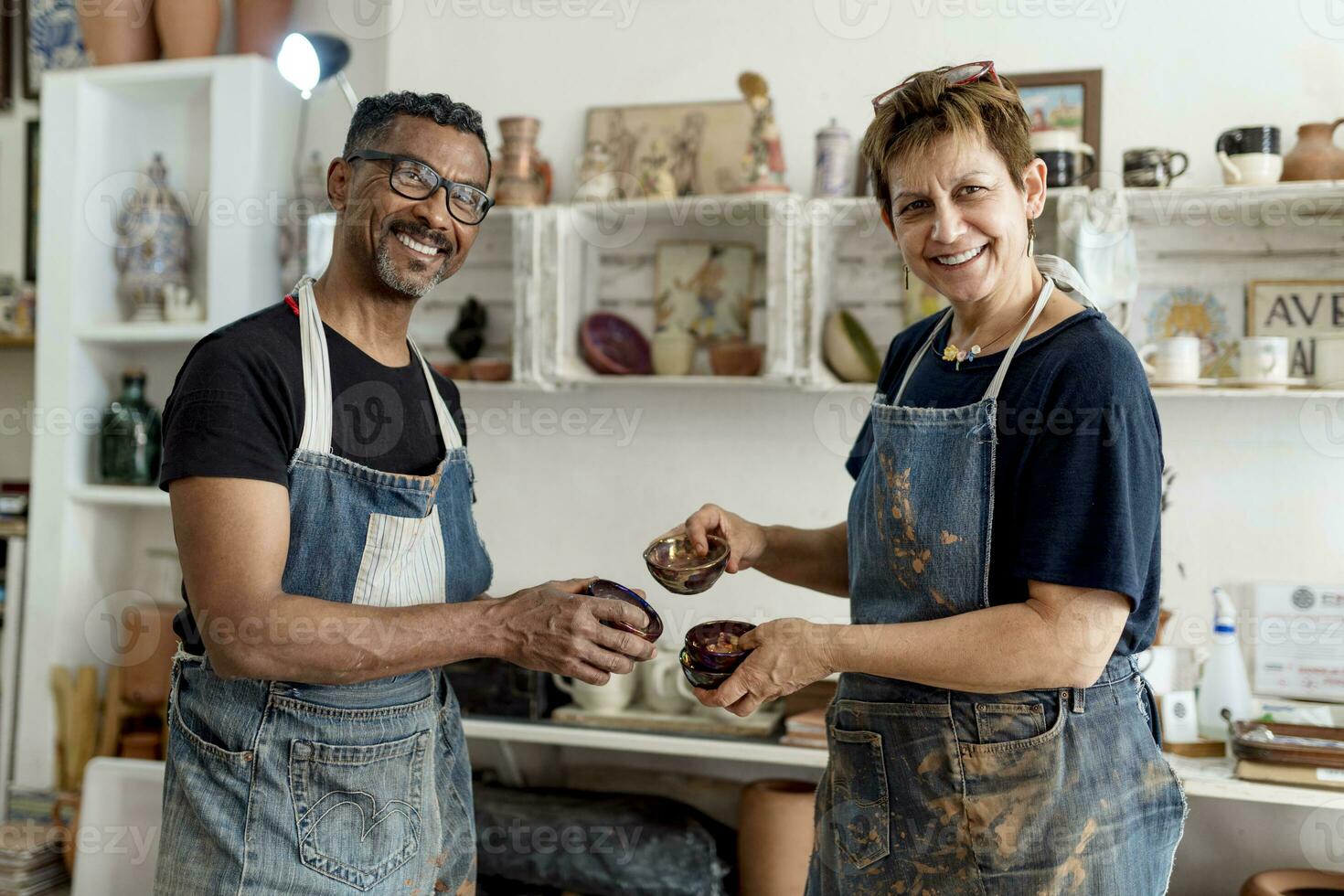 Smiling coworkers holding ceramics while standing in workshop photo