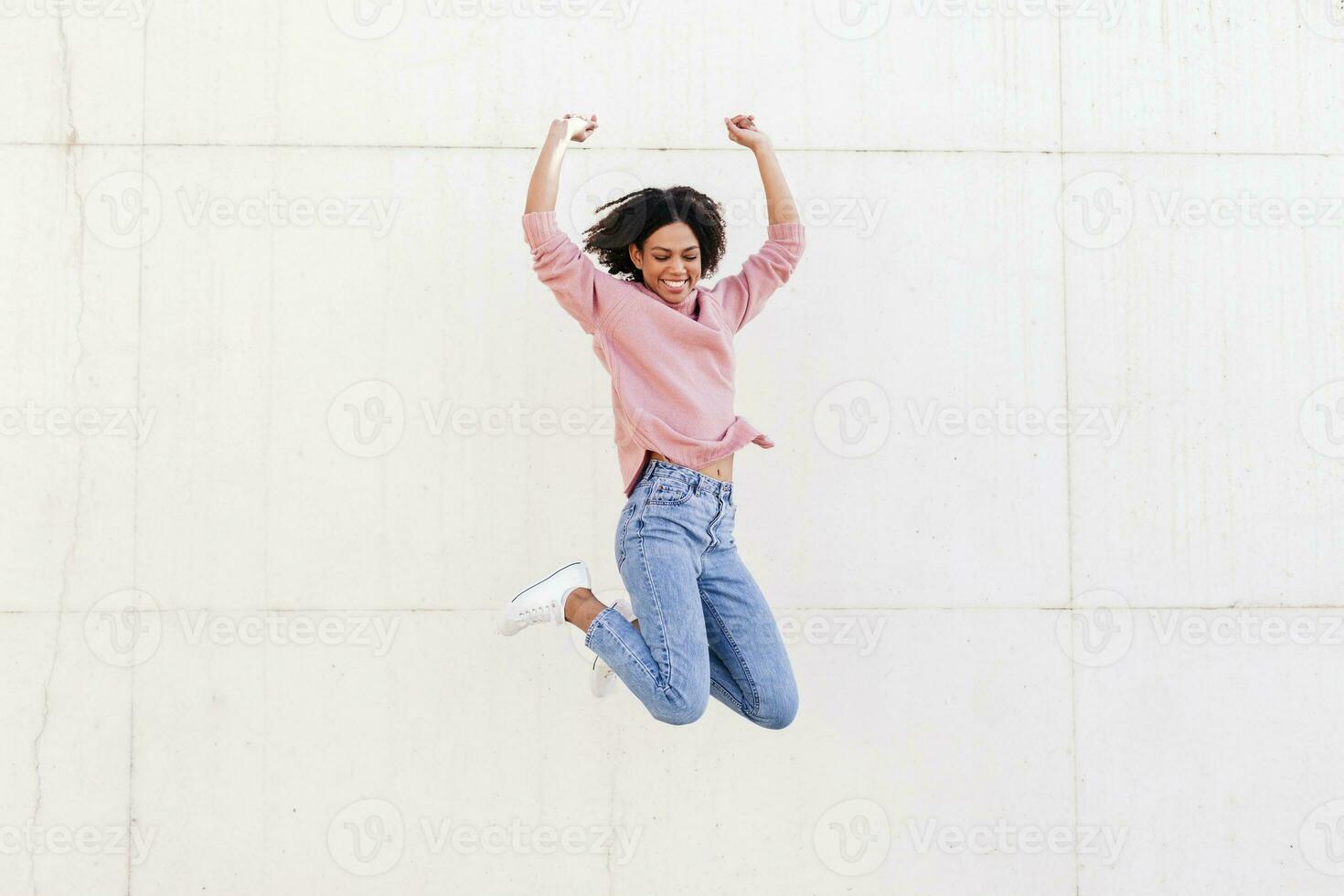 Happy young woman jumping in the air against light background photo