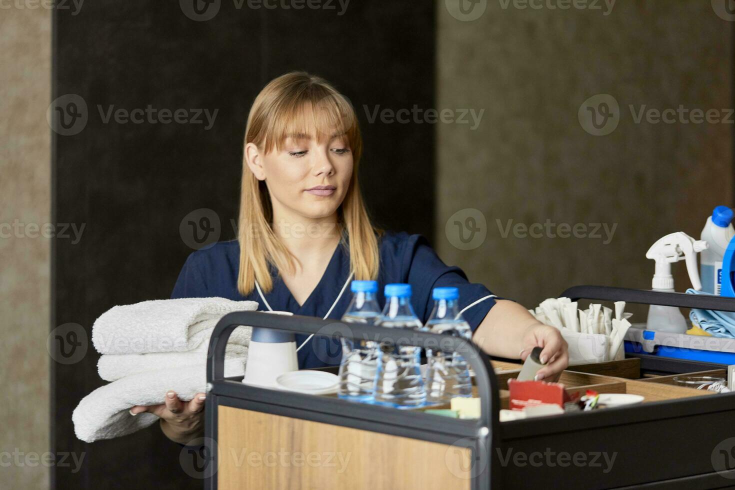 Chambermaid holding towels while standing with push scooter against wall in hotel photo