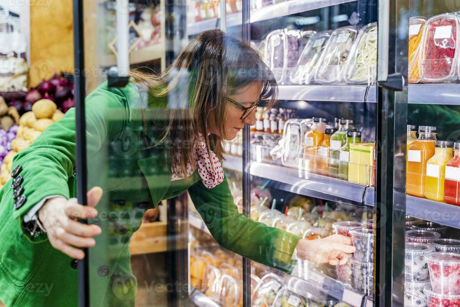 Woman taking packaged berries from cooling shelf in organic store photo