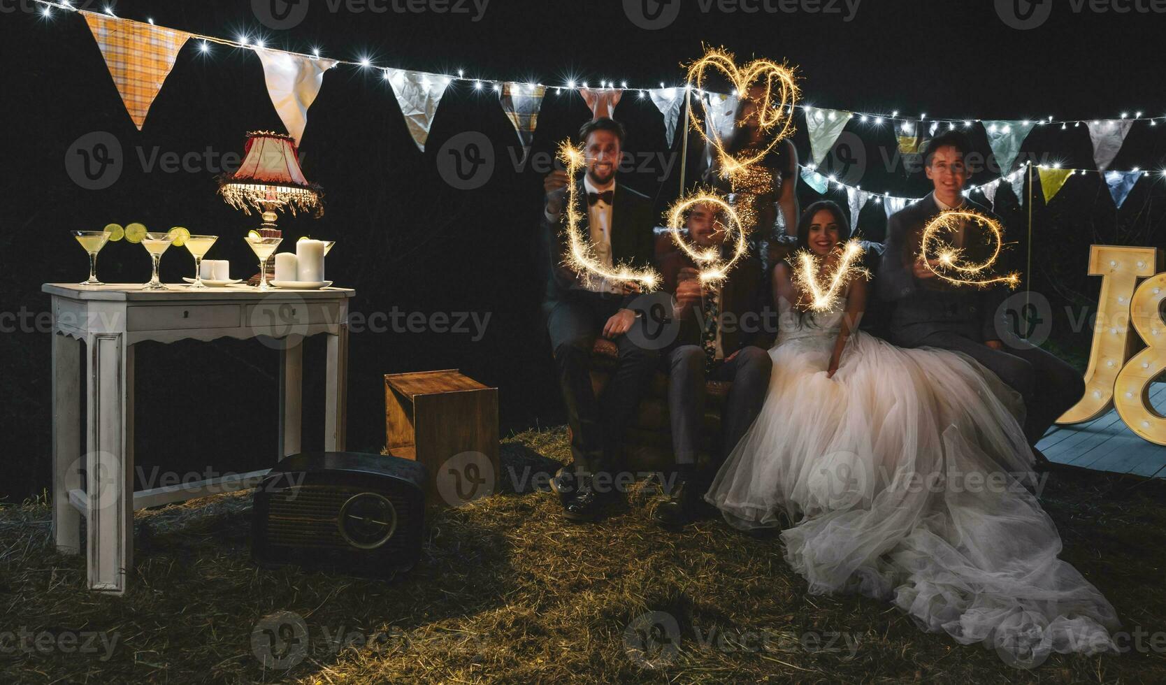 Boda Pareja y amigos haciendo el palabra 'amar' con bengalas en un noche fiesta al aire libre foto