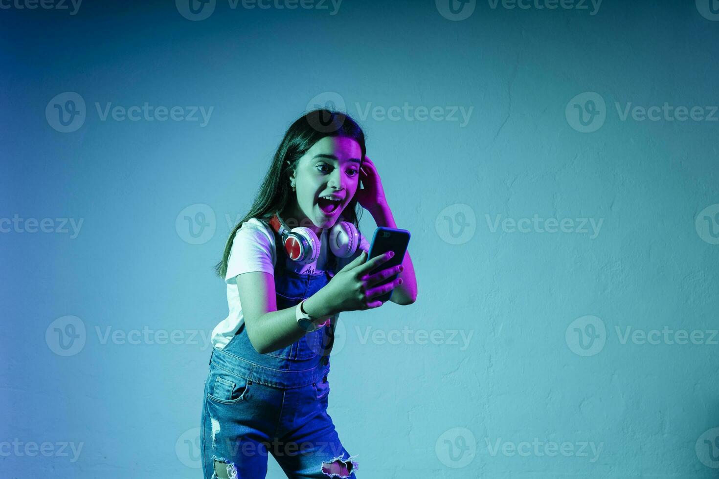 Excited girl looking at smart phone while standing against blue background photo