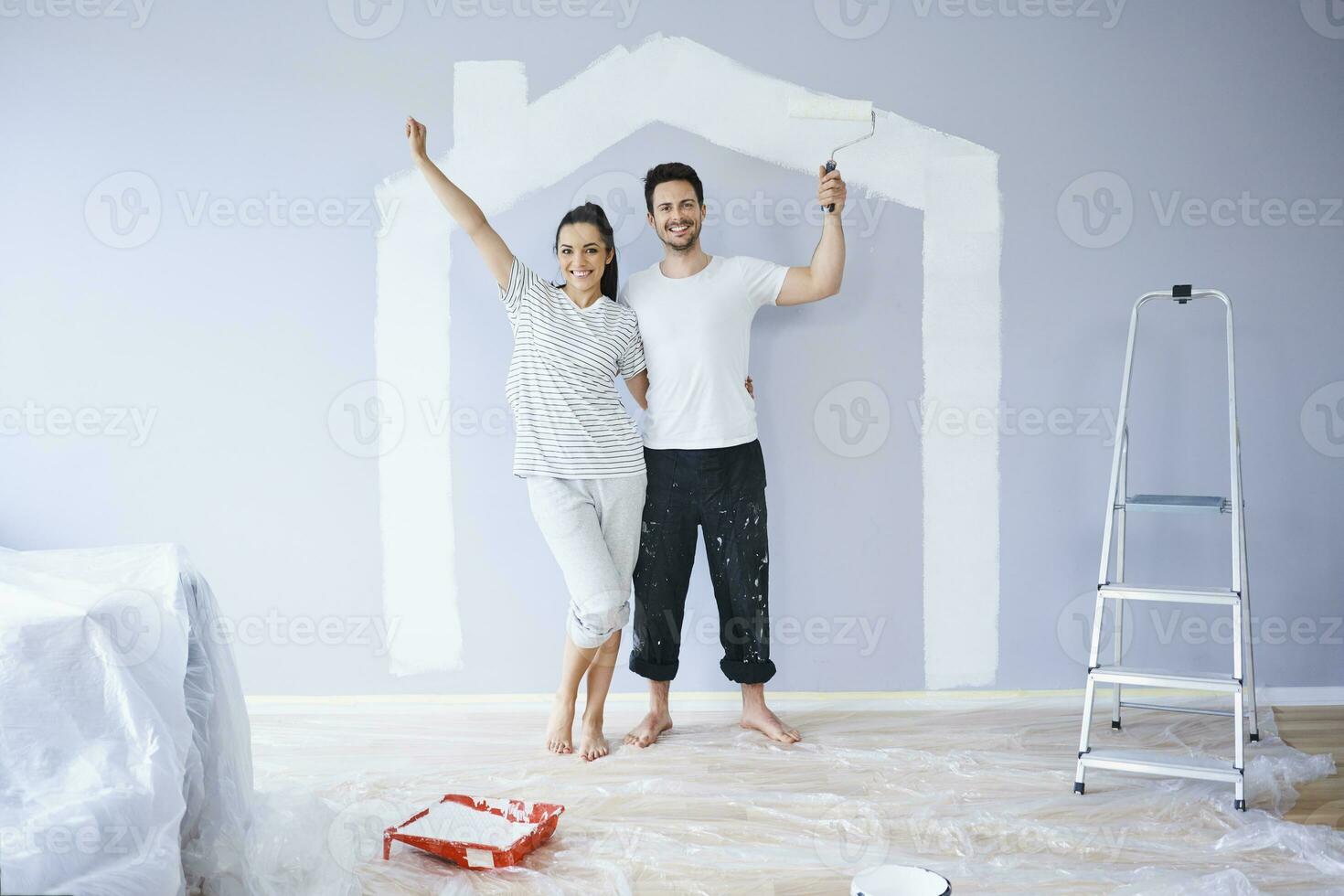 Portrait of cheerful couple painting in new apartment with house shape on wall photo