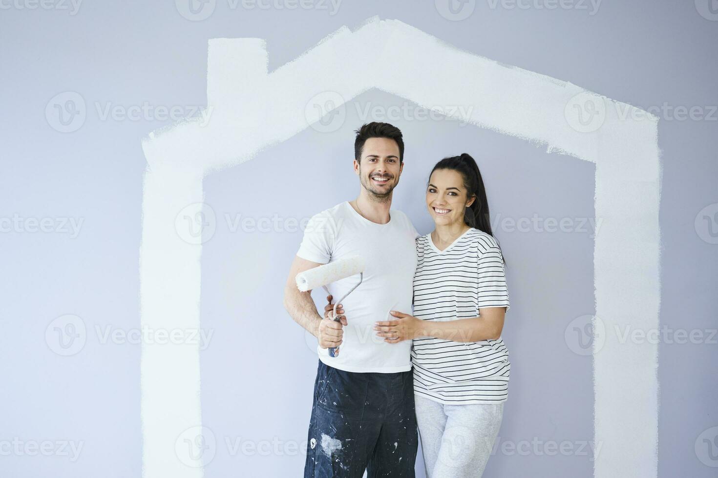 Portrait of happy couple painting in new apartment with house shape on wall photo